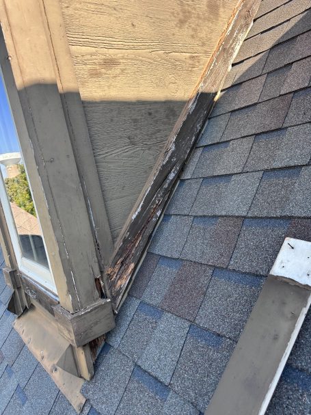 Damaged Gable Detail of a roof showing shingles and a wooden edge with peeling paint.